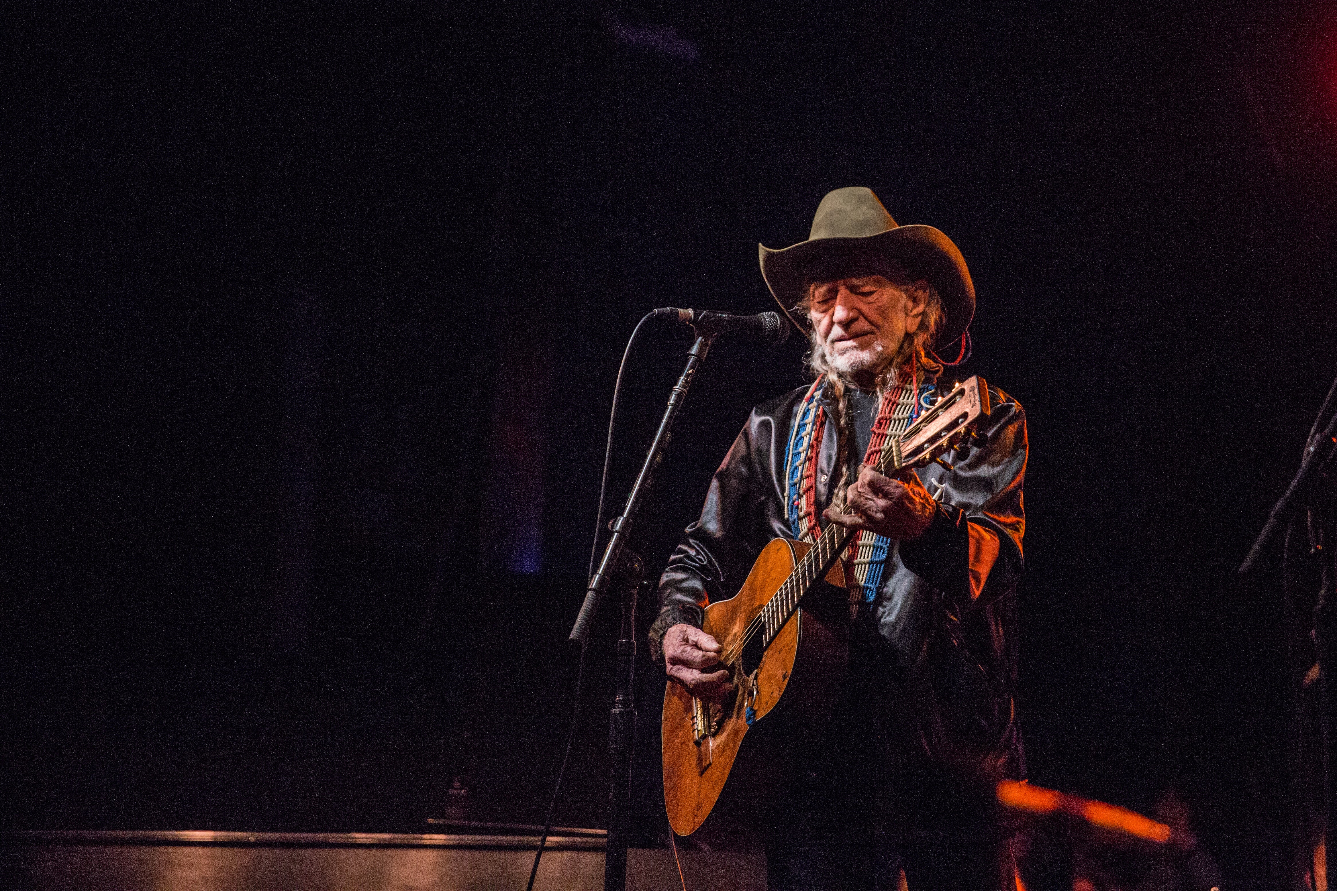 Willie Nelson in cowboy hat playing guitar on stage with microphone