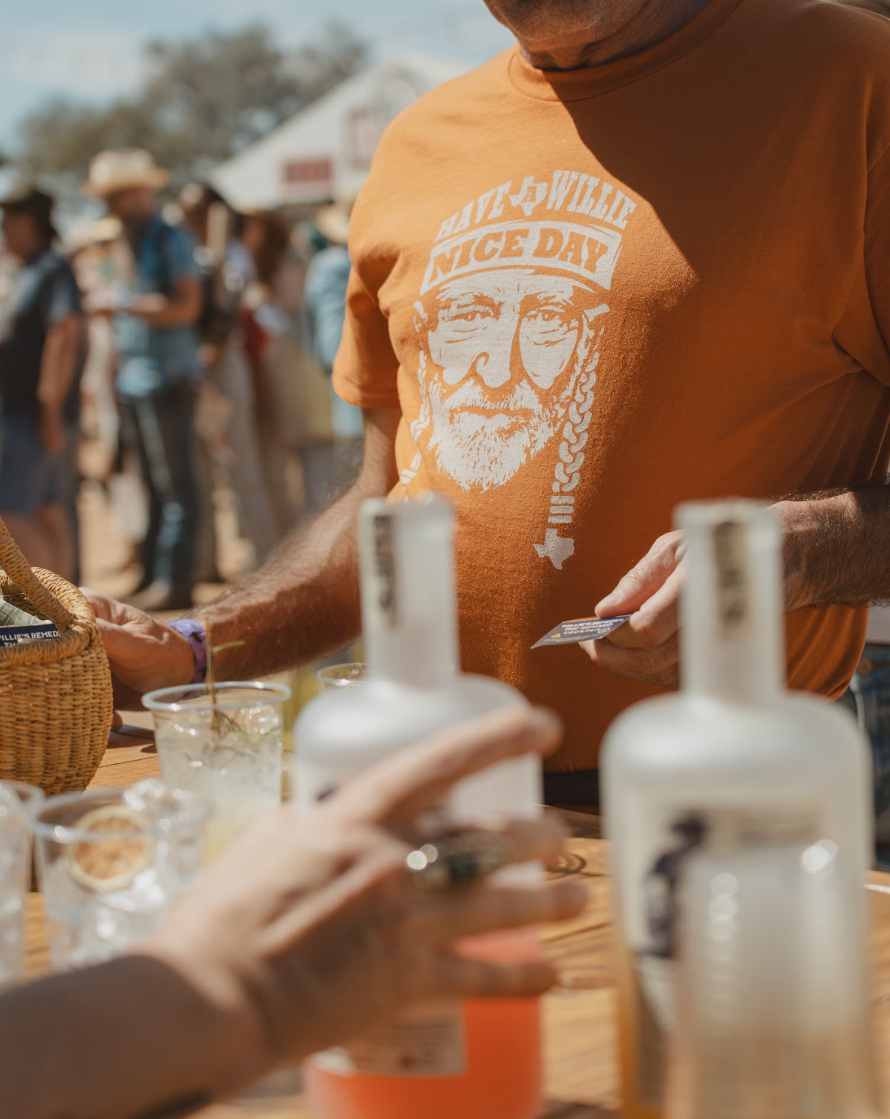 Person wearing a t-shirt with a graphic design saying Have a Willie Nice Day at an outdoor event.