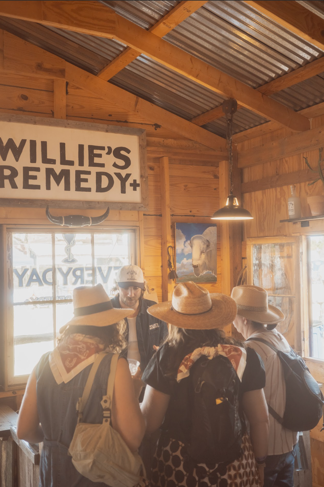 Group of people in a rustic interior with 'Willie's Remedy+' sign.