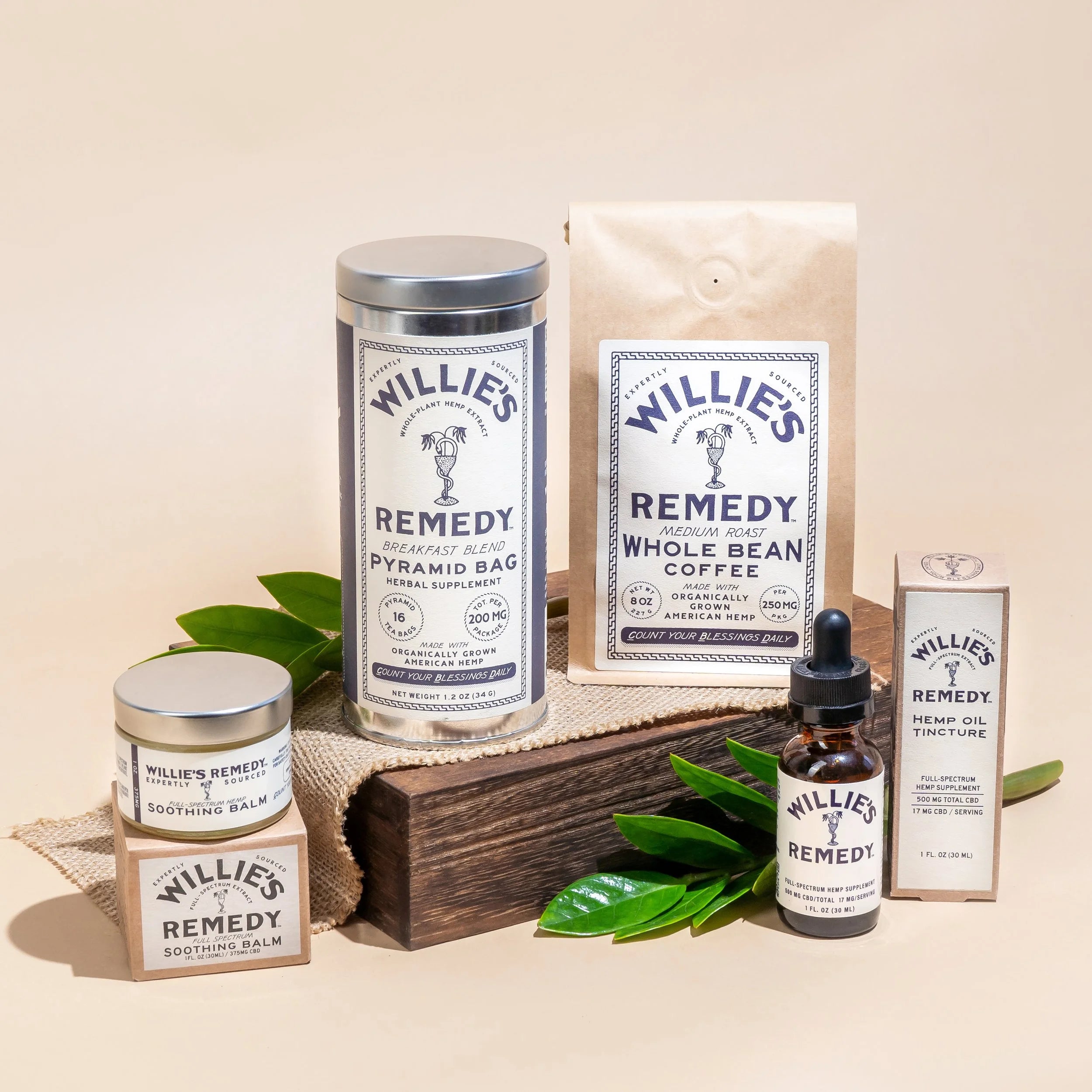 Collection of Willie's Remedy products including a canister, coffee package, balm, and tincture on a beige background.