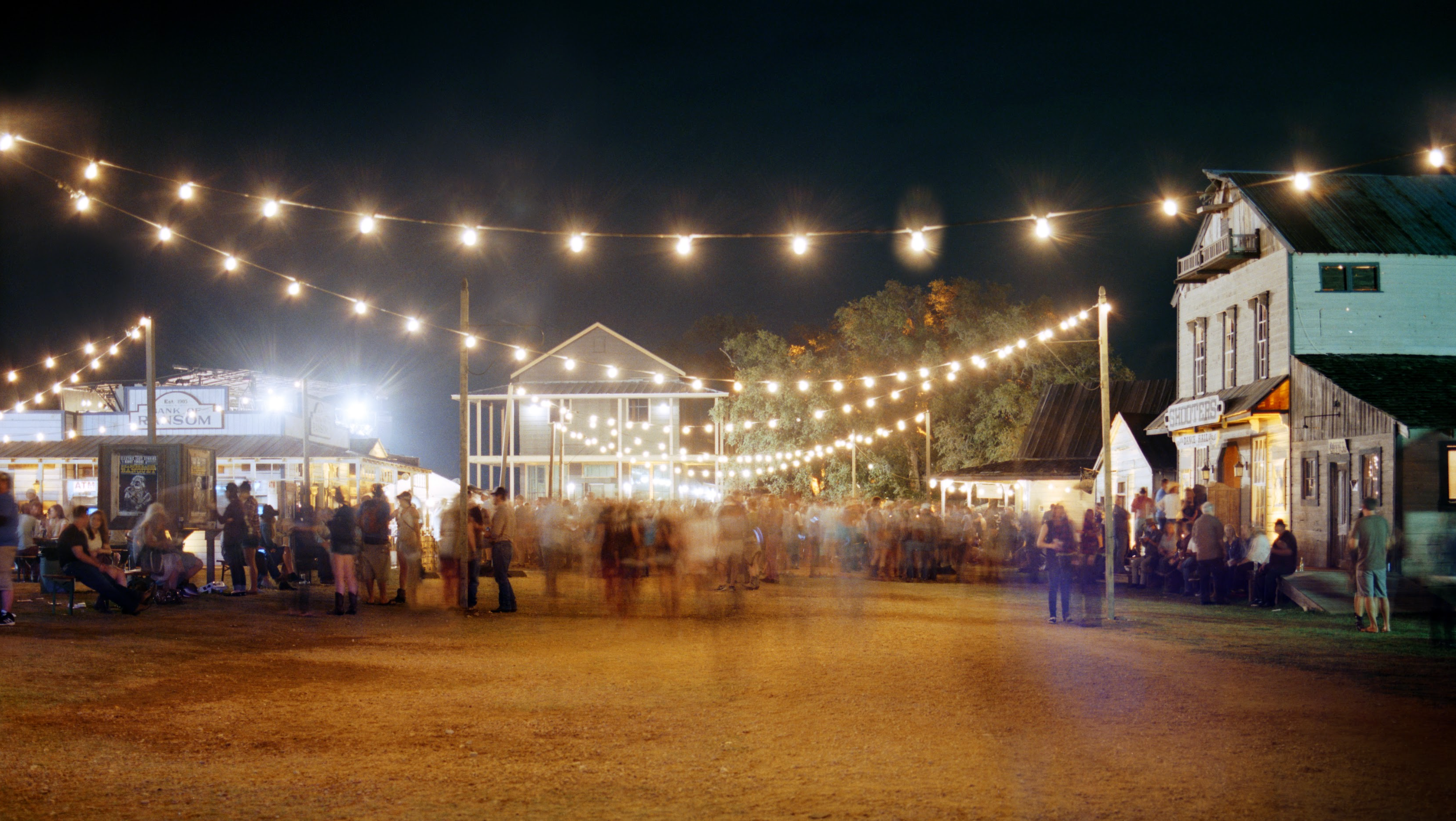 Outdoor event at night with string lights and people milling about.